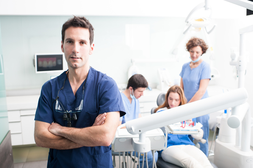 A portrait of a dentist with his team working in the background A portrait of a dentist with his team working in the background